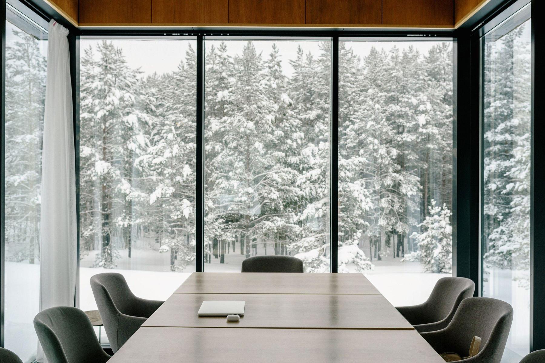 Tomt møterom med langbord og store vinduer mot en snødekt furuskog